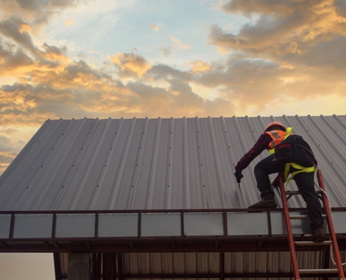 Image of a worker climbing on a metal commercial roof.