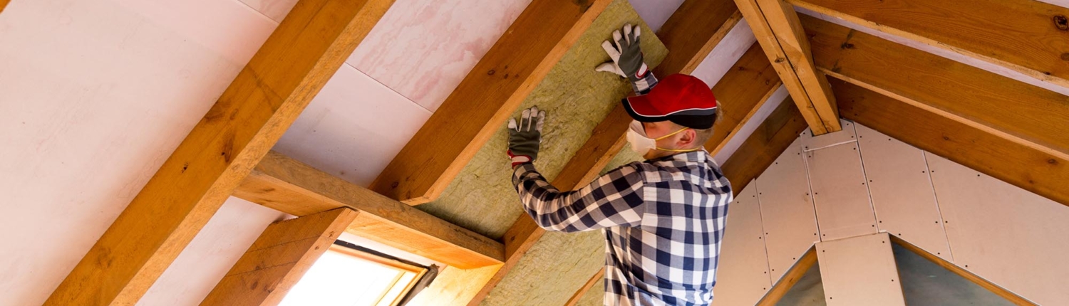Side view of a man in a red hat installing insulation on the inside of a roof